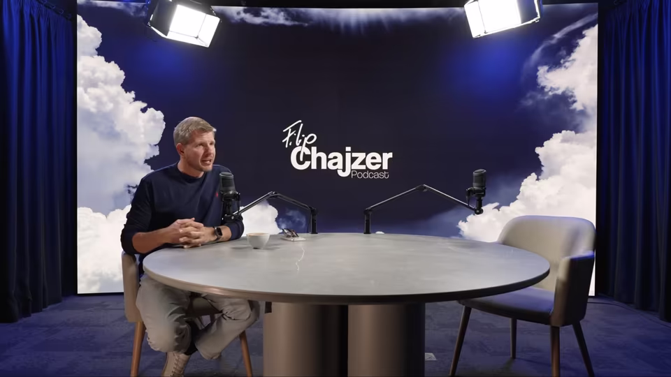 Kadr z nagrania opinii: Filip Chajzer przy stole w studiu, w tle ekran LED z logo jego podcastu