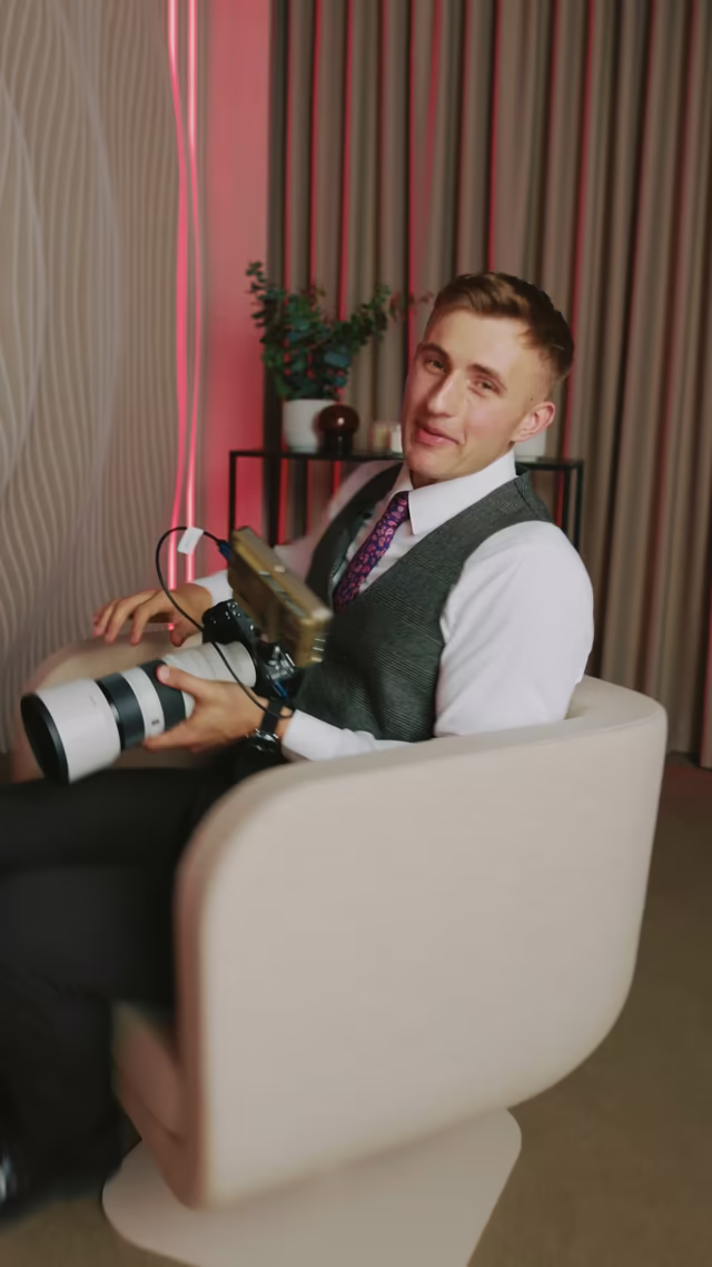 Kadr z rolki: mężczyzna z aparatem siedzi w fotelu w strefie wypoczynkowej studia